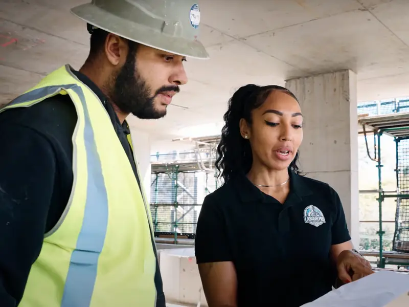 Two Labour Pro Group team members in hard hat and branded polo reviewing a job sheet on a concrete construction site