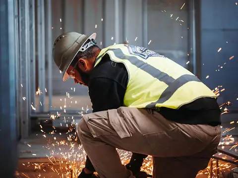 Ticketed worker in hi-vis and hard hat using a grinder on a construction site